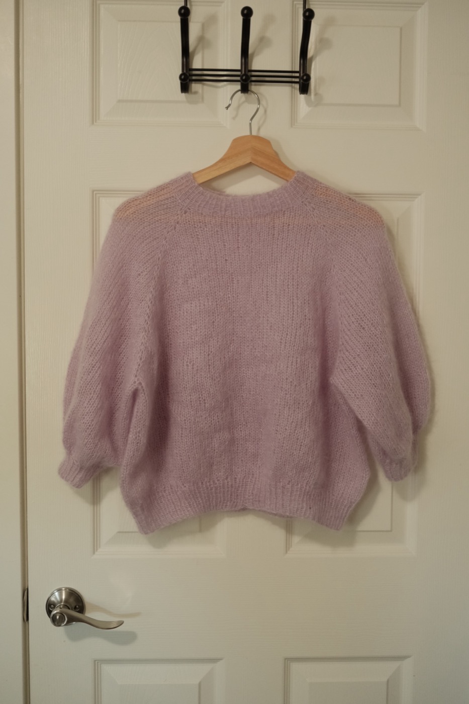 Back view of a lavender mohair sweater hanging on a wooden hanger.